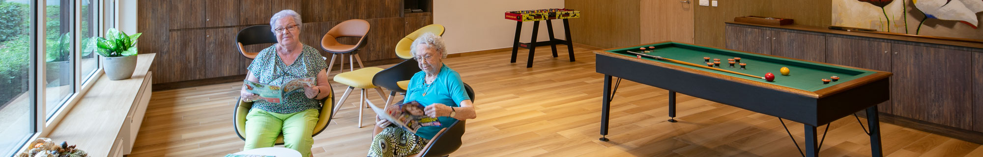 Seniorenzorg Philippus Neri twee senioren dames lezen een managzine in de leefruimte